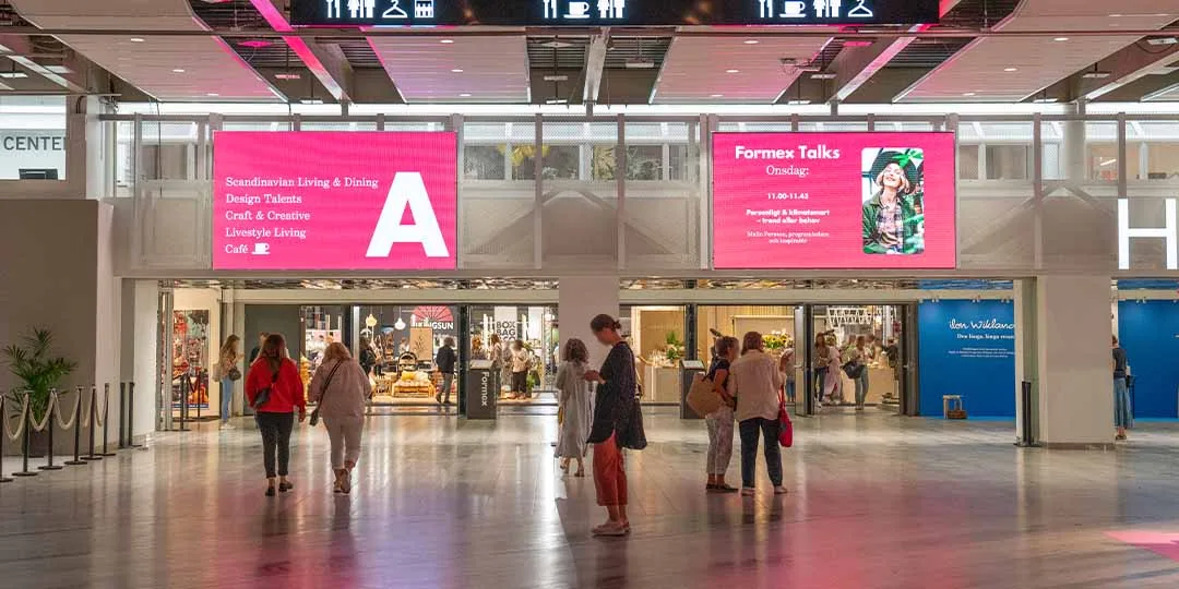 HeA1-2 (1)_1080x540px large pink digital screens leading into Hall A at Stockholmsmässan. People moving in front of the screens on their way to an exhibition