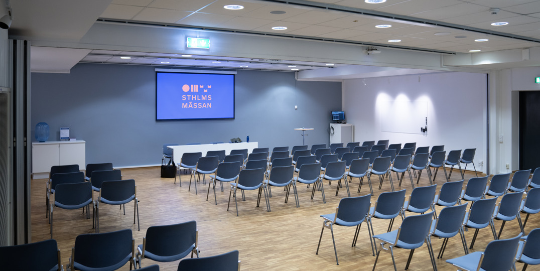 Konferenssal K18+K19 med stolar riktade mot scen och skärm på Stockholmsmässan.