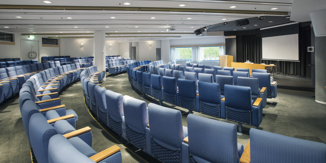 Sal K21 med blå stolsrader riktade mot scen och presentationsduk.