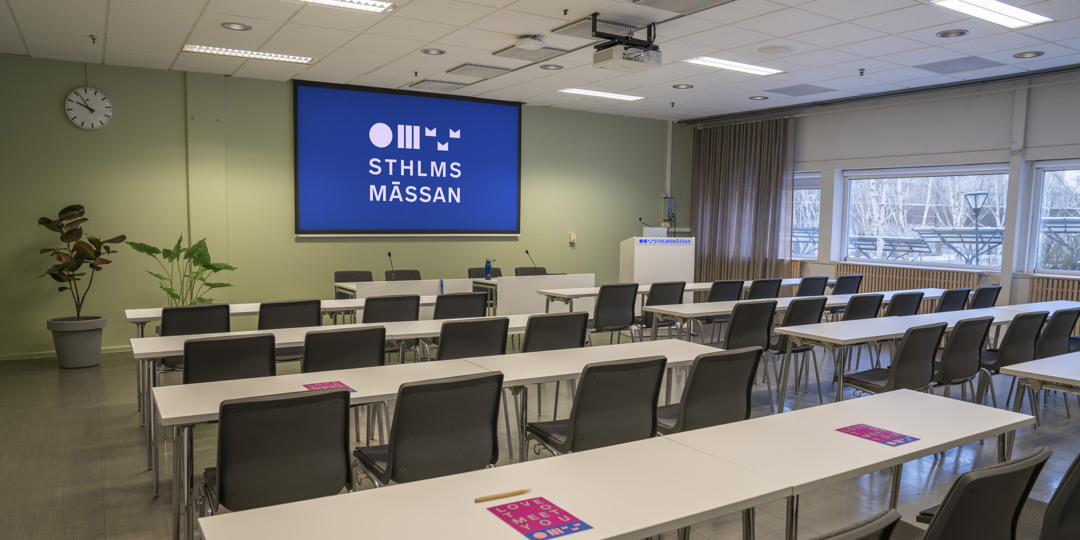 Konferensrum K-22 med långbord, stolar och stor presentationsskärm på Stockholmsmässan.