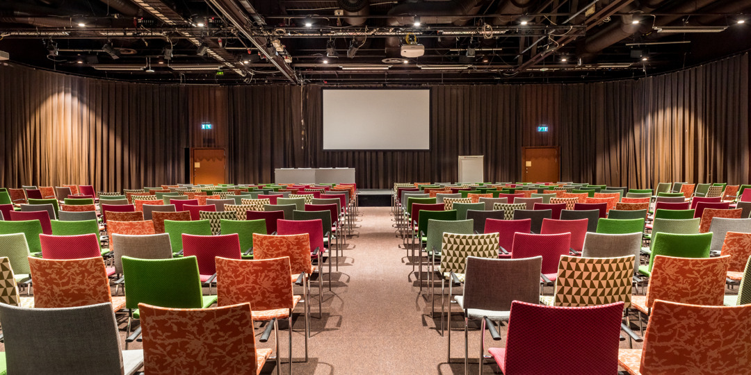 Föreläsningssal och konferensrum med färgglada stolar och scen, redo för presentation eller konferens.