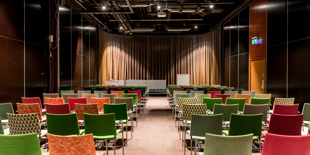 T3 är ett mindre konferensrum med färgglada stolar, scen och whiteboard, redo för möte eller presentation.