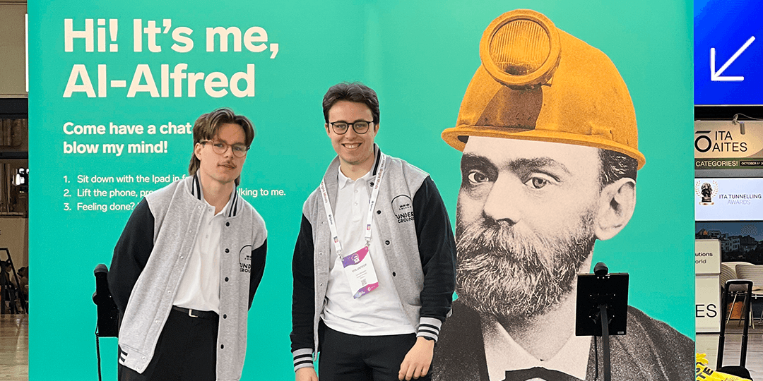 world-tunnel-congress-2025-hosts-entretorget-alfred-university-stockholm-fair-1080x540px Two student hosts from local Stockholm universities in front of a wall with Alfred Nobel during the World Tunnel Congress 2025 at Stockholmsmässan.