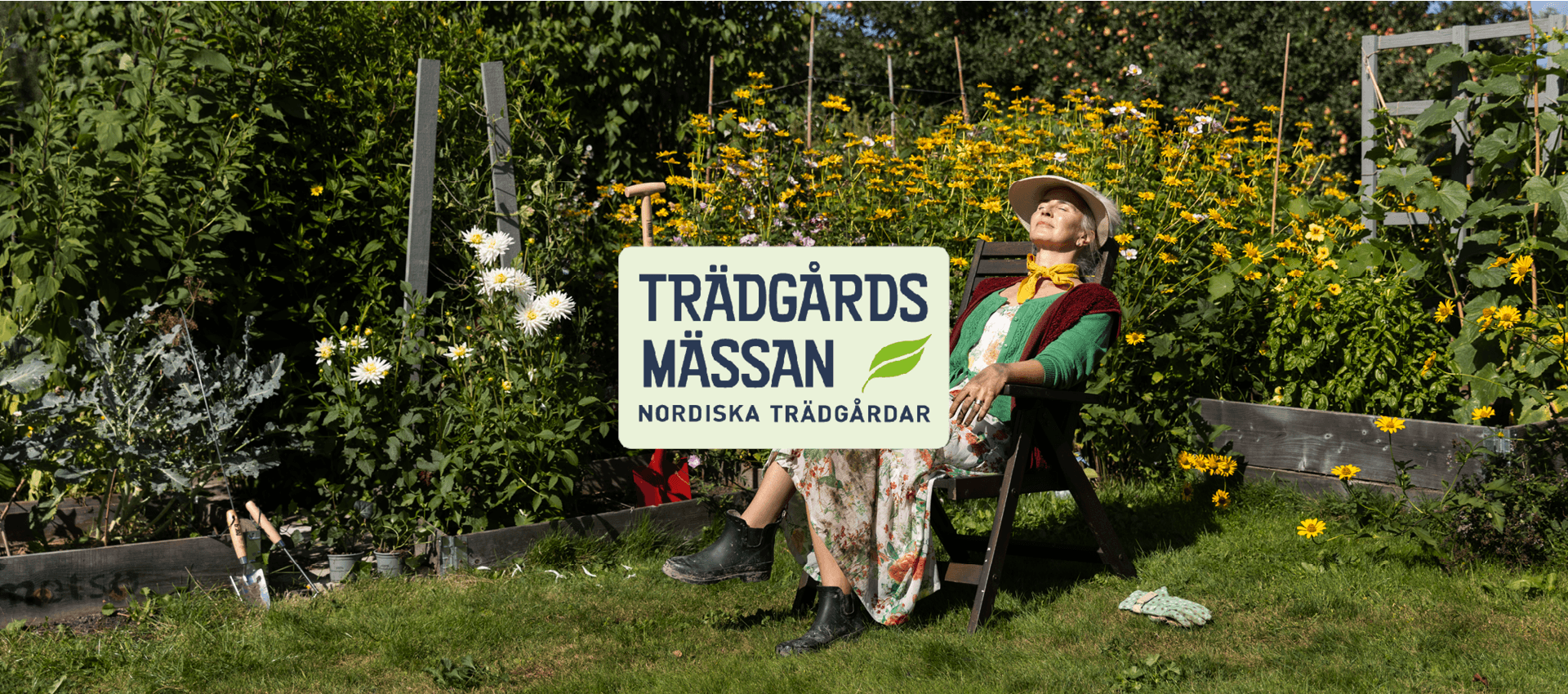 Kvinna vilar i trädgårdsstol bland blommor, med solhatt och kaffekopp i solen.