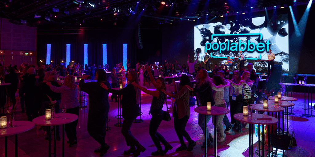 Deltagare dansar i ring till livemusik på ett event med festlig belysning under en kickoff i Victoriahallen på Stockholmsmässan