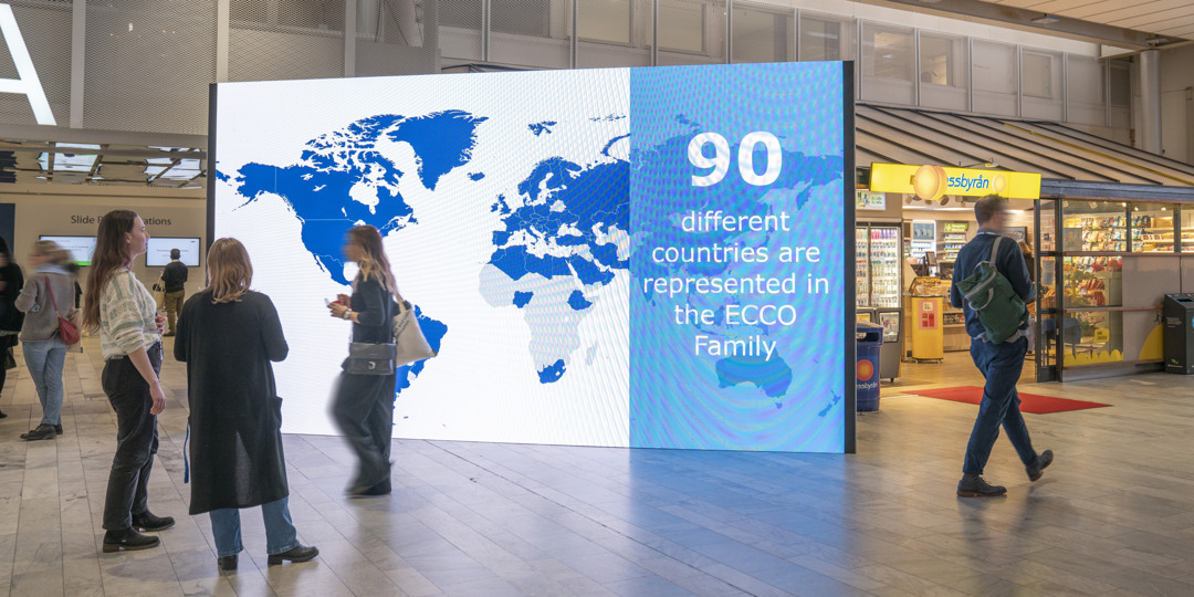 Visitors passing a large digital map showcasing ECCO’s global presence in 90 countries during a congress at Stockholmsmässan.