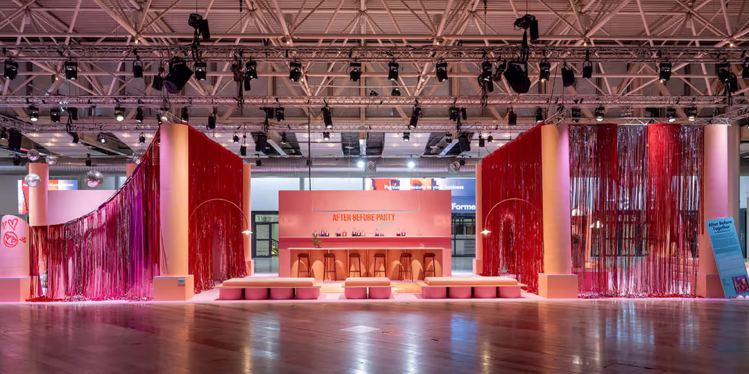 Rosa och röd eventyta inomhus med bar, sittplatser och dekorativa draperier under ett tak med många spotlights, skyltad ”After Before Party”.