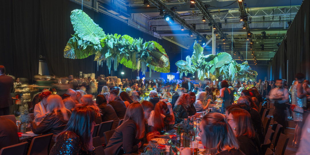 Gala dinner with long tables, hanging decorations and guests in conversation and motion during an event at Stockholmsmässan.