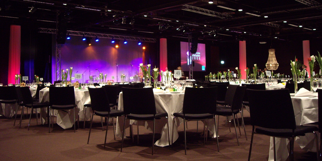 Set round tables, stage and coloured lighting ahead of an event at Stockholmsmässan.
