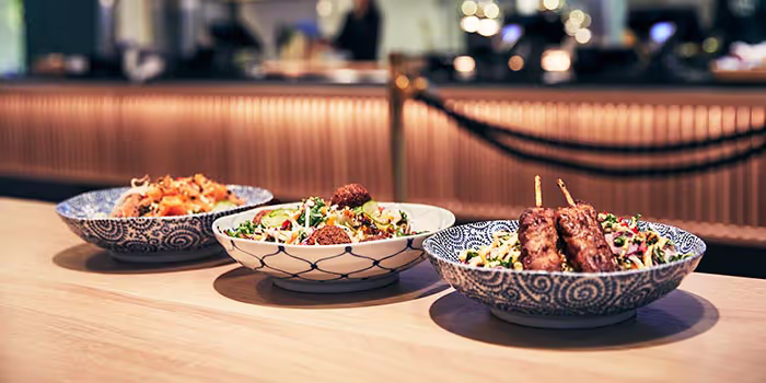 Tre skålar med upplagd mat på en bardisk i restaurangmiljö.