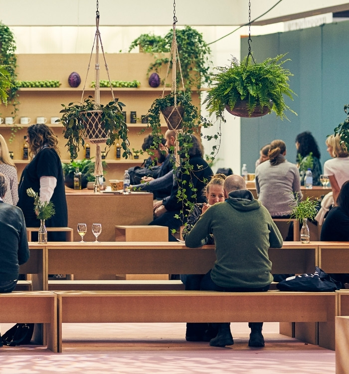 Människor som minglar i en trämonter med gröna växter. English: People mingling in a wooden exhibition stand with green plants.