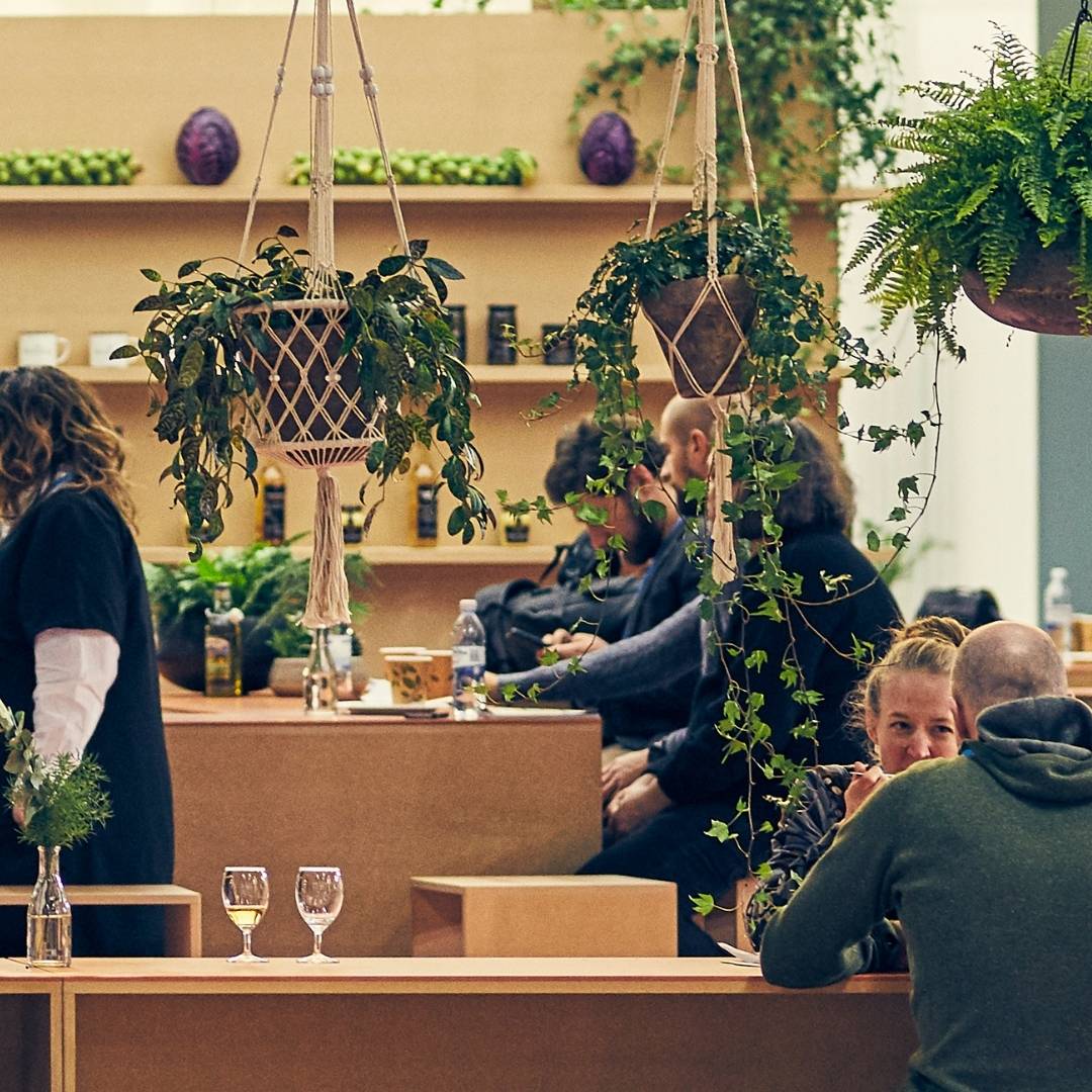 People mingling in a wooden exhibition stand with green plants. English: People mingling in a wooden exhibition stand with green plants. 